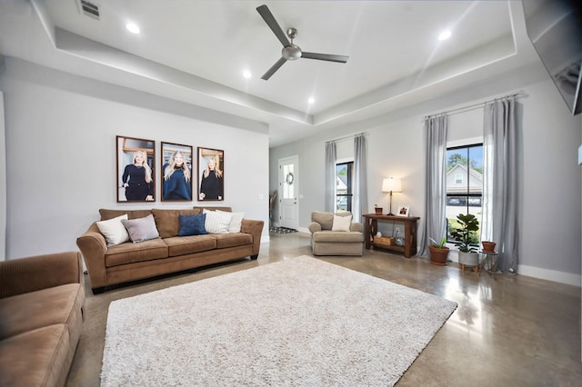 living area featuring concrete flooring, a raised ceiling, a ceiling fan, baseboards, and visible vents
