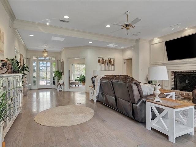 living room featuring ceiling fan, light wood-type flooring, crown molding, and a brick fireplace