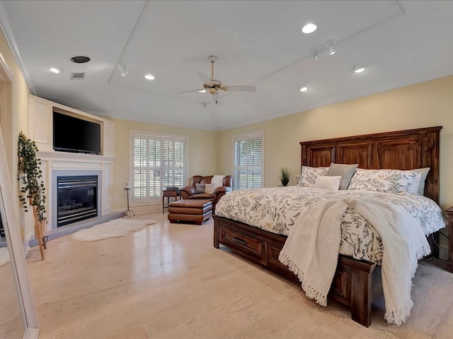 bedroom featuring ceiling fan, ornamental molding, a fireplace, and light hardwood / wood-style flooring