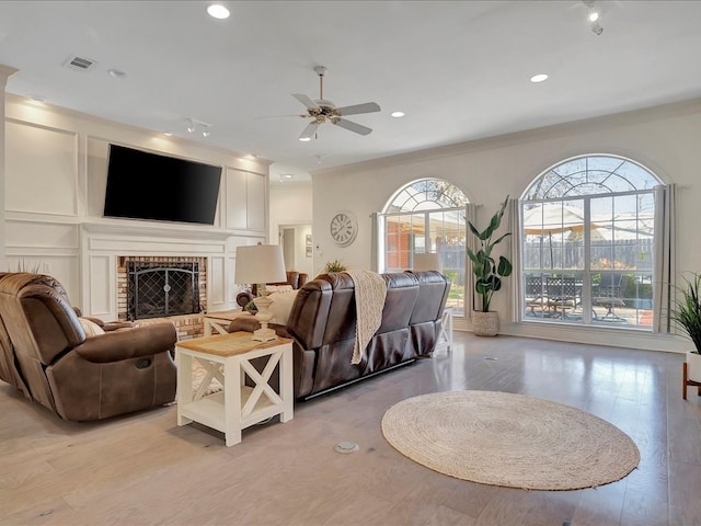 living room with a fireplace, ceiling fan, light hardwood / wood-style flooring, and ornamental molding