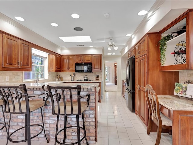 kitchen featuring a skylight, ceiling fan, light stone countertops, a breakfast bar area, and stainless steel refrigerator