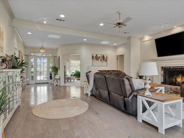 living room featuring a fireplace, light hardwood / wood-style floors, ceiling fan, and crown molding