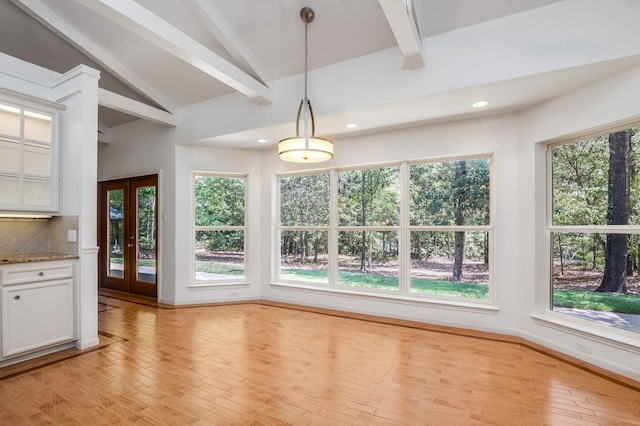 unfurnished dining area featuring french doors, light wood-type flooring, lofted ceiling with beams, and a healthy amount of sunlight