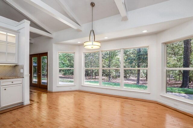 unfurnished dining area featuring french doors, light wood-type flooring, lofted ceiling with beams, and a healthy amount of sunlight