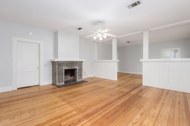 unfurnished living room with light wood finished floors, ceiling fan, a brick fireplace, and visible vents