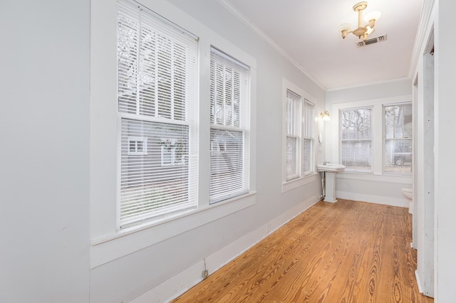 interior space featuring baseboards, light wood-style floors, visible vents, and crown molding