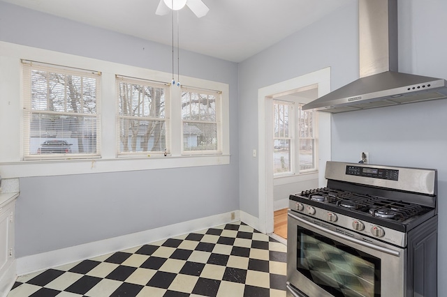 kitchen with dark floors, wall chimney range hood, stainless steel gas range, and baseboards