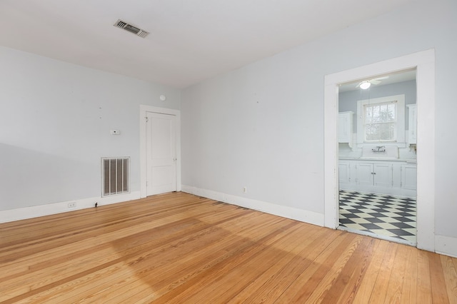 unfurnished room with light wood finished floors, a sink, visible vents, and baseboards