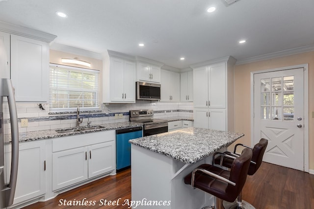 kitchen featuring appliances with stainless steel finishes, dark wood-type flooring, sink, white cabinets, and a center island