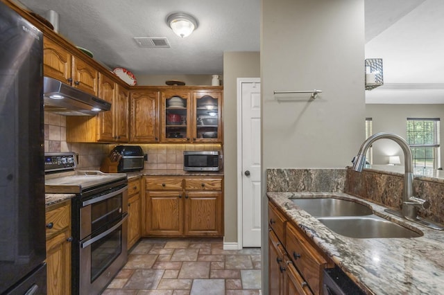 kitchen featuring sink, decorative backsplash, a textured ceiling, light stone counters, and stainless steel appliances