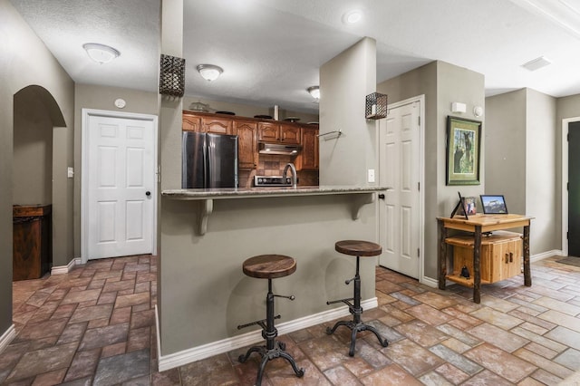 kitchen with sink, a kitchen bar, a textured ceiling, and stainless steel refrigerator