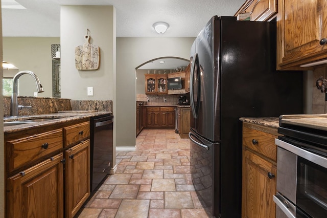 kitchen with a textured ceiling, sink, dark stone counters, and black appliances