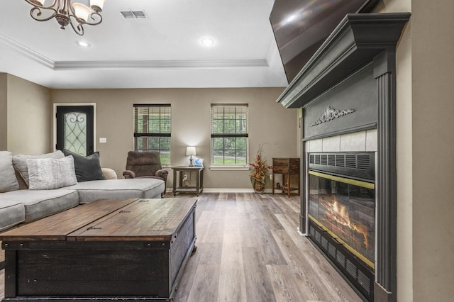 living room with a tray ceiling, a fireplace, wood-type flooring, and an inviting chandelier