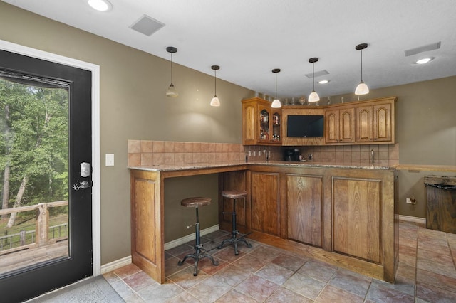 bar featuring decorative backsplash, light stone countertops, and hanging light fixtures