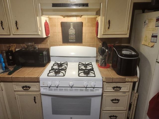 kitchen with under cabinet range hood, tasteful backsplash, white gas range oven, tile countertops, and black microwave