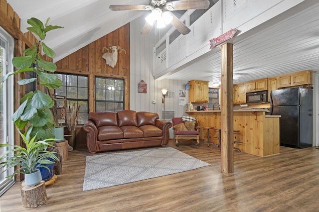 living room featuring hardwood / wood-style flooring, high vaulted ceiling, a healthy amount of sunlight, and wooden walls