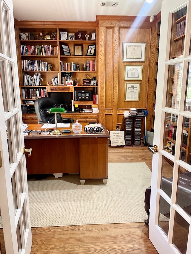 home office with wood-type flooring, french doors, and wood walls