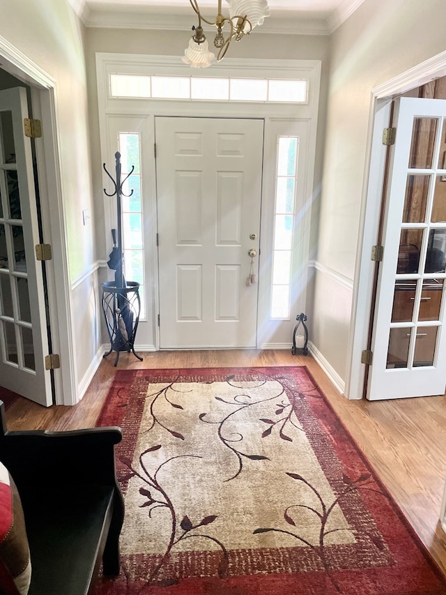 foyer entrance with crown molding, hardwood / wood-style floors, and an inviting chandelier