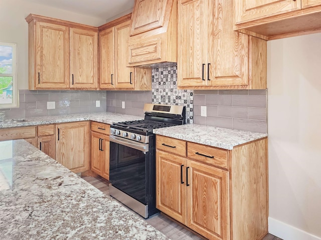 kitchen featuring decorative backsplash, light wood-type flooring, light stone countertops, and stainless steel gas range oven