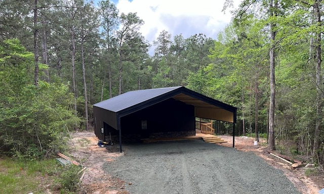 garage featuring a detached carport, driveway, and a view of trees