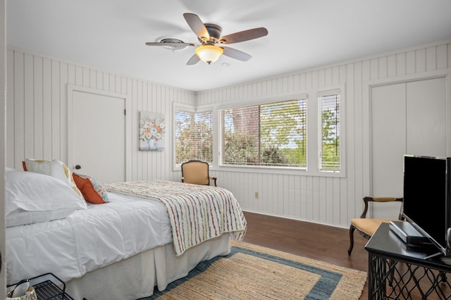 bedroom with ceiling fan, wooden walls, and wood-type flooring