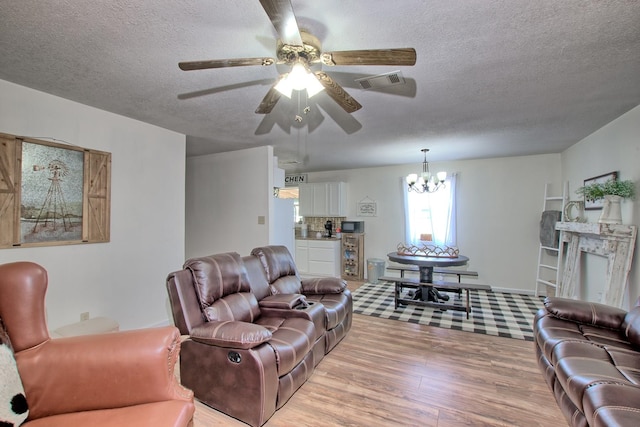 living room featuring light hardwood / wood-style flooring, ceiling fan with notable chandelier, and a textured ceiling