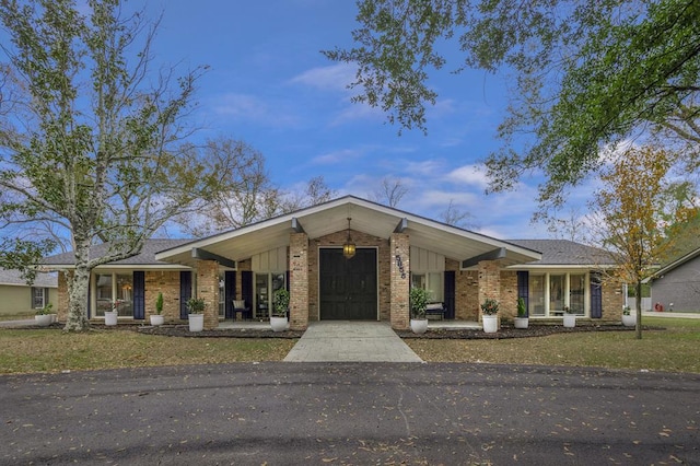 mid-century modern home with an attached garage, driveway, a front lawn, brick siding, and a porch