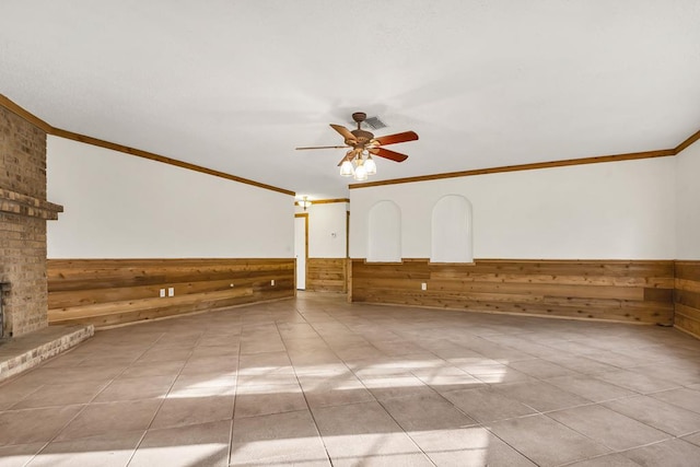 unfurnished living room featuring crown molding, light tile patterned flooring, ceiling fan, and wood walls