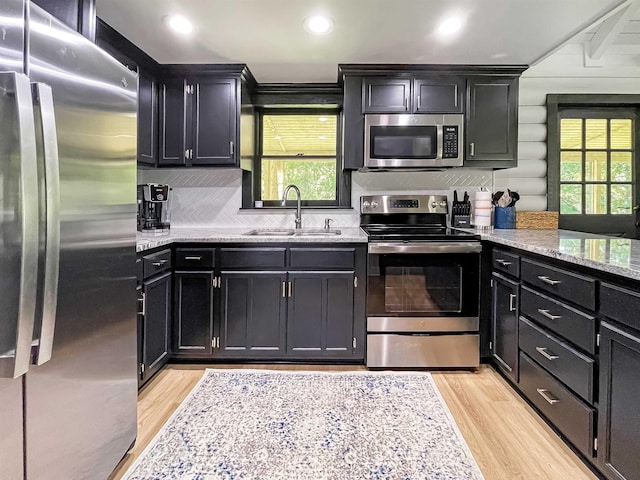 kitchen with light stone countertops, sink, stainless steel appliances, tasteful backsplash, and light wood-type flooring