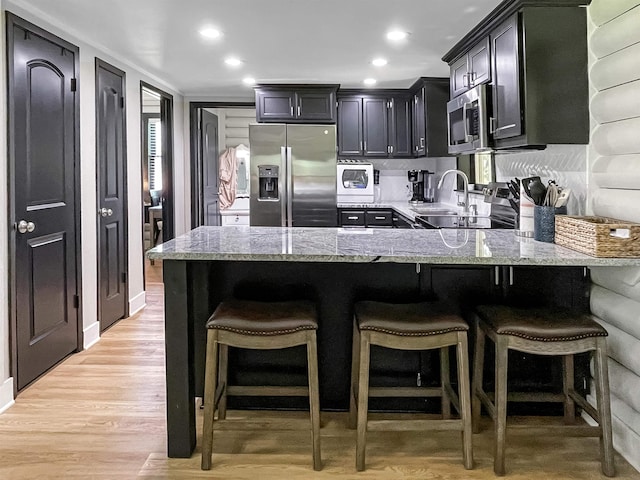 kitchen with light stone countertops, kitchen peninsula, a breakfast bar, appliances with stainless steel finishes, and light wood-type flooring