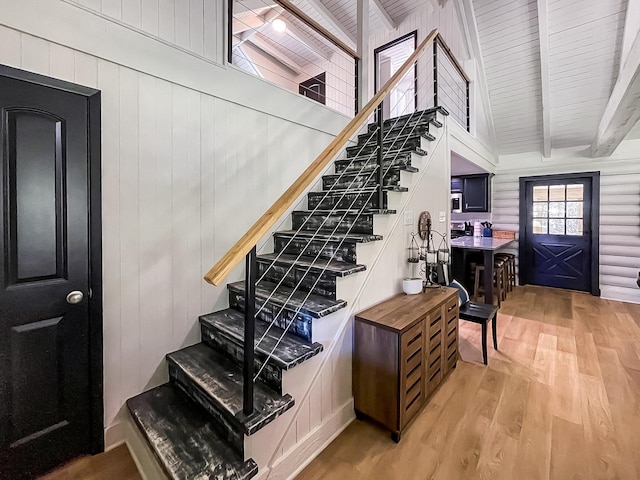 staircase with hardwood / wood-style floors, beam ceiling, and wooden walls