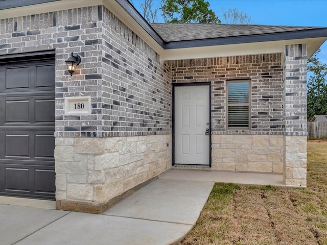 property entrance featuring an attached garage, stone siding, a shingled roof, and brick siding