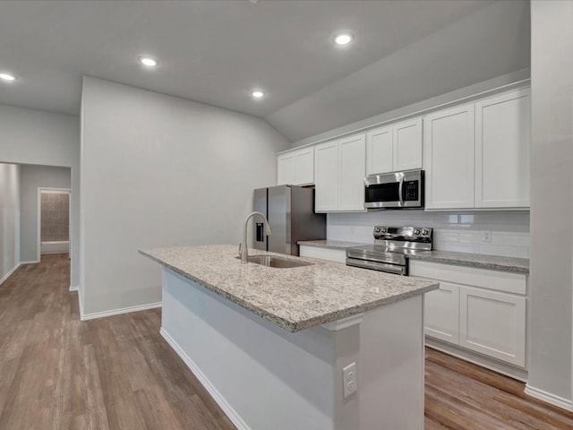 kitchen with appliances with stainless steel finishes, a center island with sink, backsplash, and wood finished floors