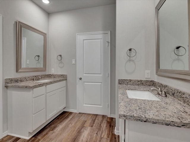 bathroom featuring wood finished floors, two vanities, a sink, and baseboards