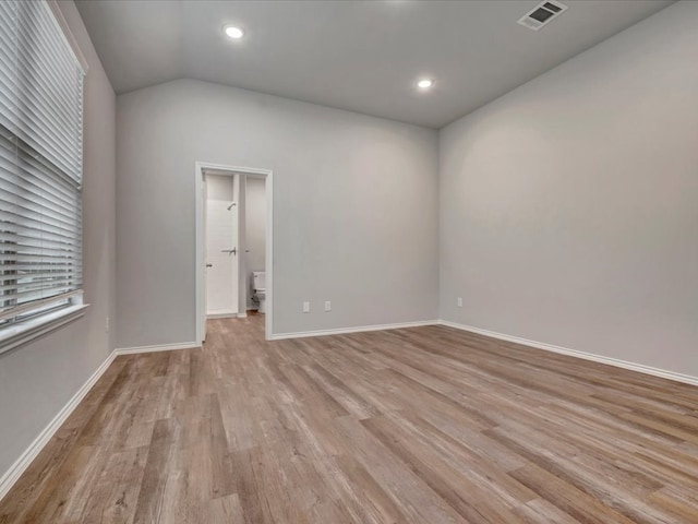 empty room featuring vaulted ceiling, light wood-style flooring, visible vents, and baseboards