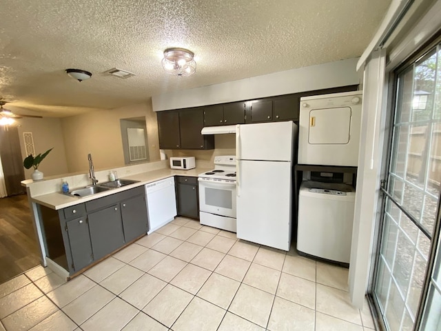 kitchen with white appliances, sink, ceiling fan, stacked washing maching and dryer, and a textured ceiling