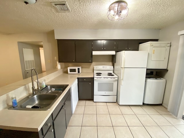 kitchen with white appliances, sink, stacked washer and dryer, light tile patterned floors, and a textured ceiling