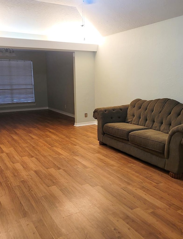 living room with vaulted ceiling, a textured ceiling, wood finished floors, and baseboards