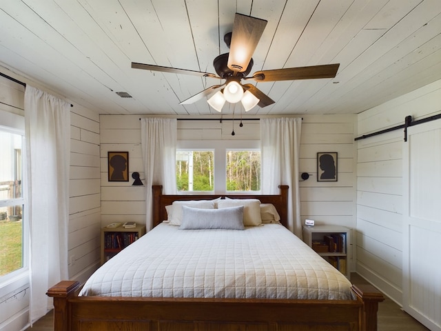 bedroom featuring a barn door, wood walls, ceiling fan, and wooden ceiling