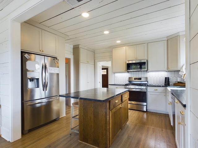 kitchen featuring a center island, a kitchen bar, appliances with stainless steel finishes, tasteful backsplash, and dark hardwood / wood-style flooring