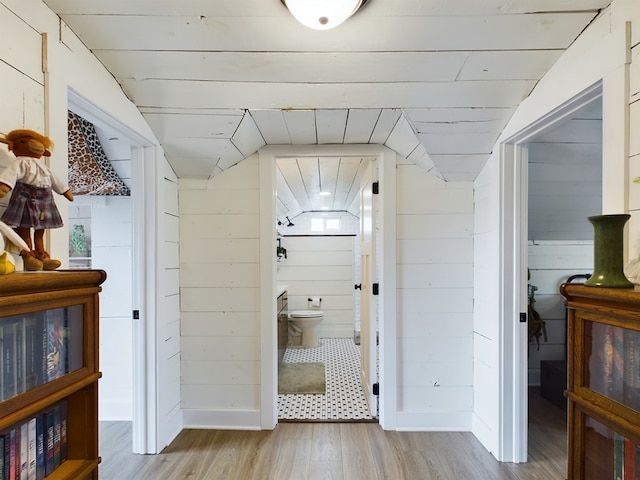 corridor featuring wood walls, light hardwood / wood-style flooring, and vaulted ceiling