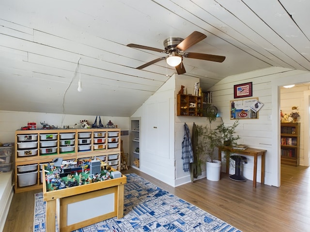 playroom featuring ceiling fan, wooden walls, wood-type flooring, and lofted ceiling