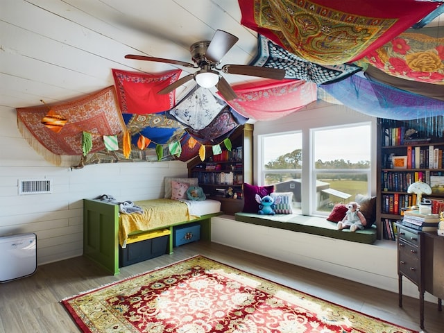 bedroom with hardwood / wood-style flooring, ceiling fan, and wooden walls