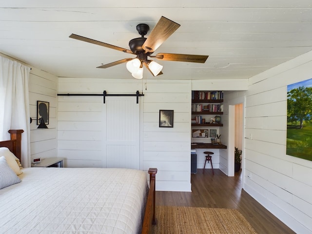 bedroom with wood walls, dark hardwood / wood-style floors, a barn door, and ceiling fan