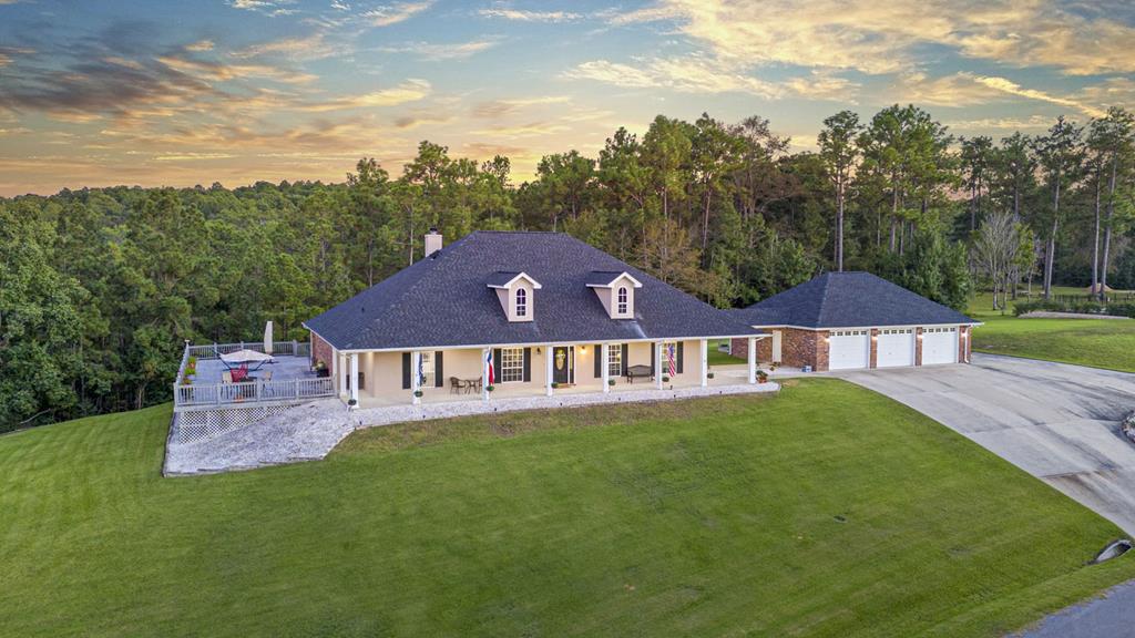 farmhouse-style home with an outbuilding, concrete driveway, a front yard, a view of trees, and a chimney