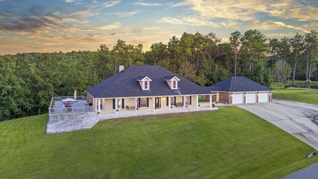 farmhouse-style home with an outbuilding, concrete driveway, a front yard, a view of trees, and a chimney