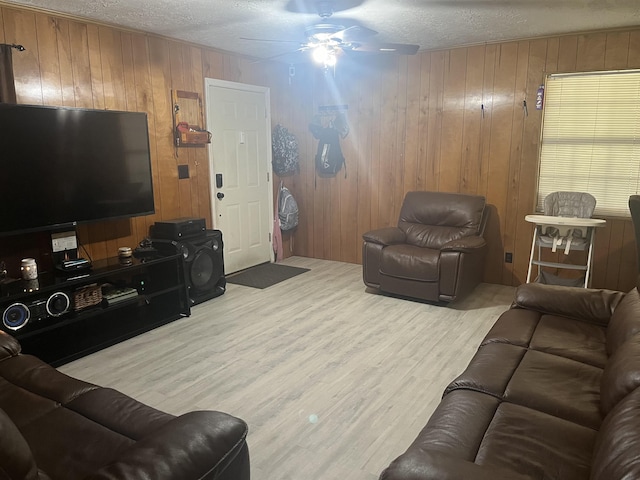 living room with a textured ceiling, light wood-type flooring, and wood walls