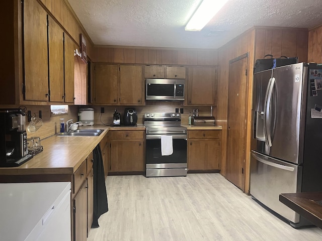 kitchen featuring decorative backsplash, appliances with stainless steel finishes, a textured ceiling, sink, and light hardwood / wood-style flooring