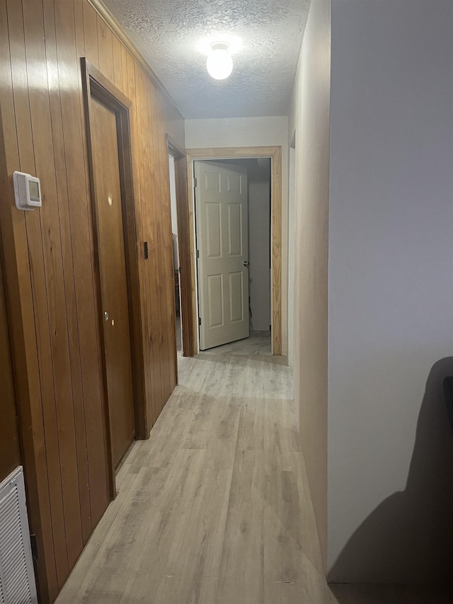 corridor with wooden walls, light hardwood / wood-style flooring, and a textured ceiling