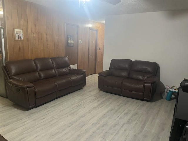 living room featuring light wood-type flooring, ceiling fan, and wooden walls